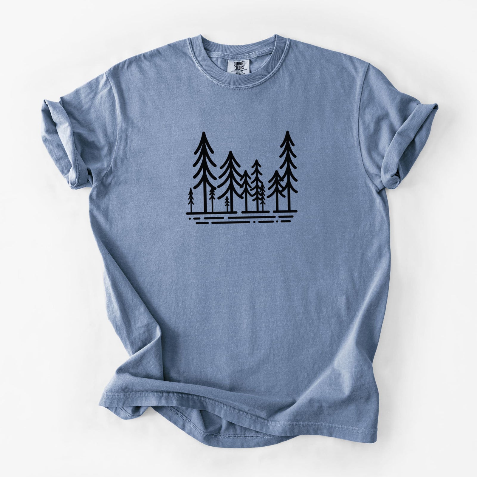Blue jean Comfort Colors t-shirt laid flat, printed with bold black line art of ten simple pine trees above horizontal lines.