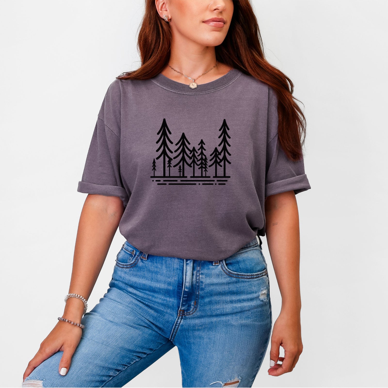 Blue jean Comfort Colors t-shirt laid flat, printed with bold black line art of ten simple pine trees above horizontal lines.