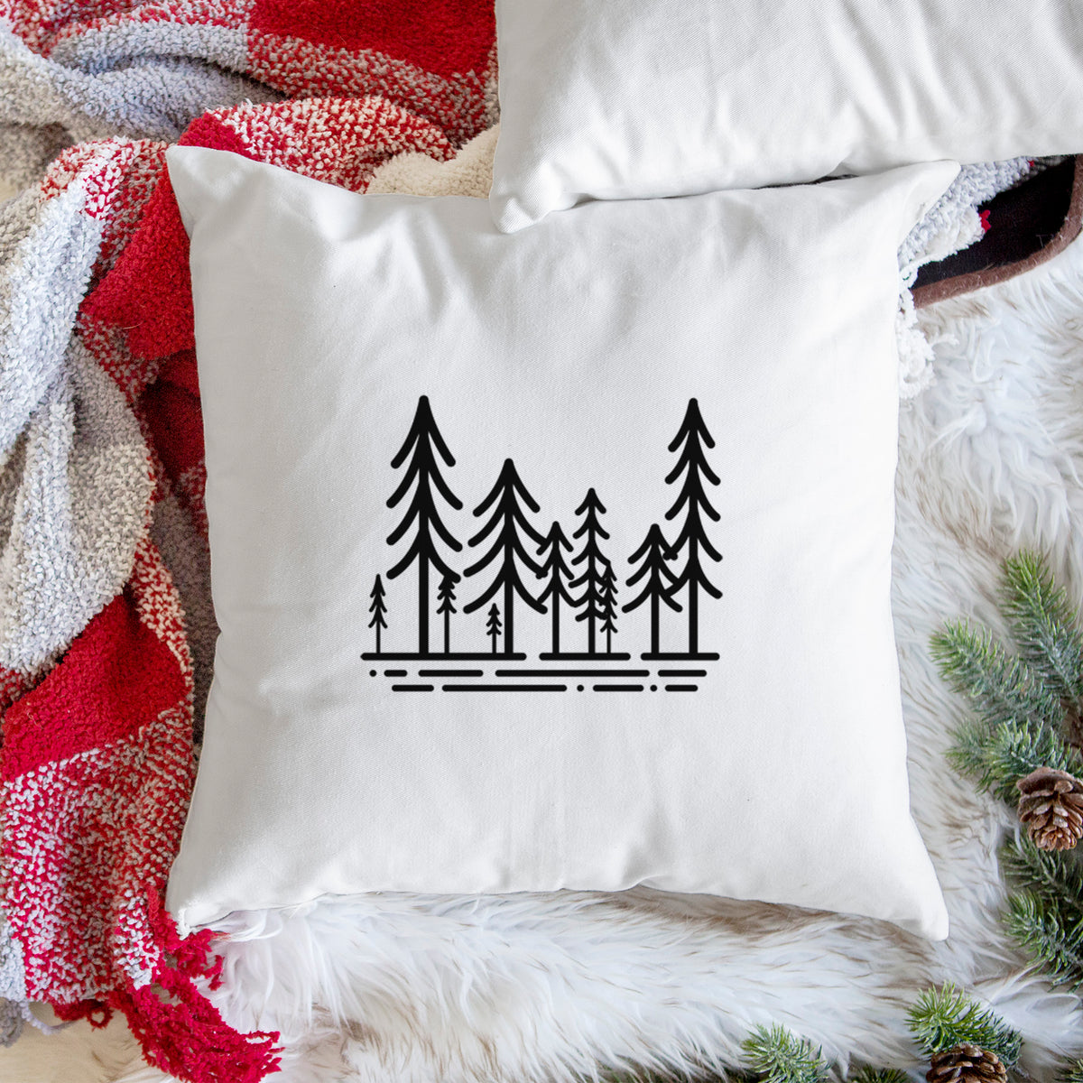 White pillow cover printed with bold black line art of ten simple pine trees above horizontal lines, on a woven chair.