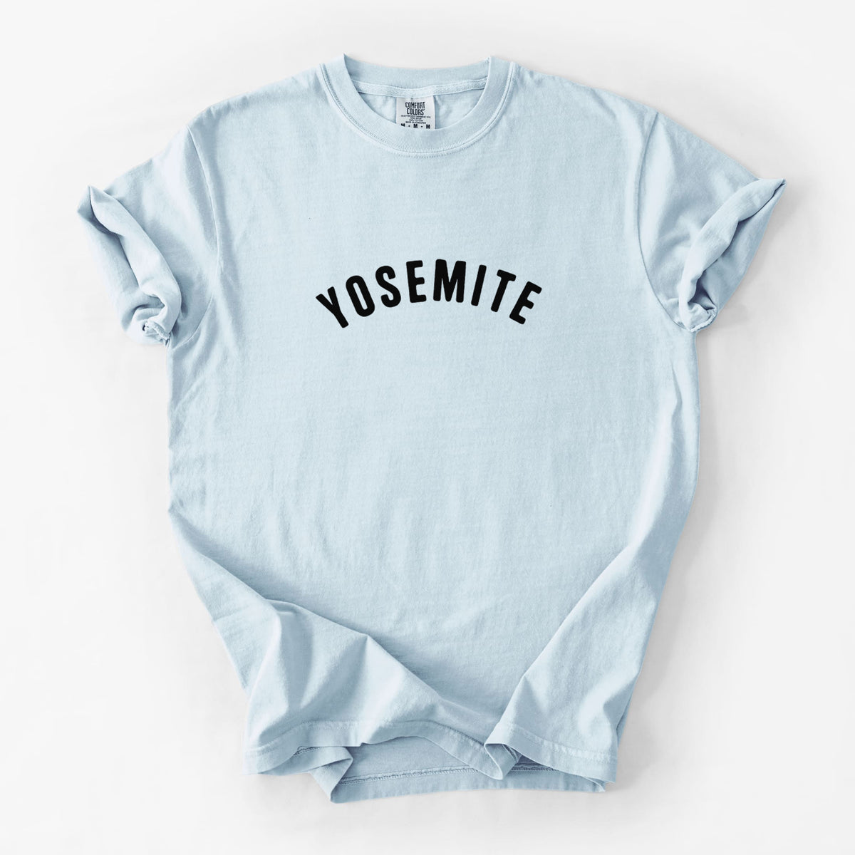Chambray blue Comfort Colors t-shirt laid flat, printed with the word Yosemite in bold black letters arched across the chest.