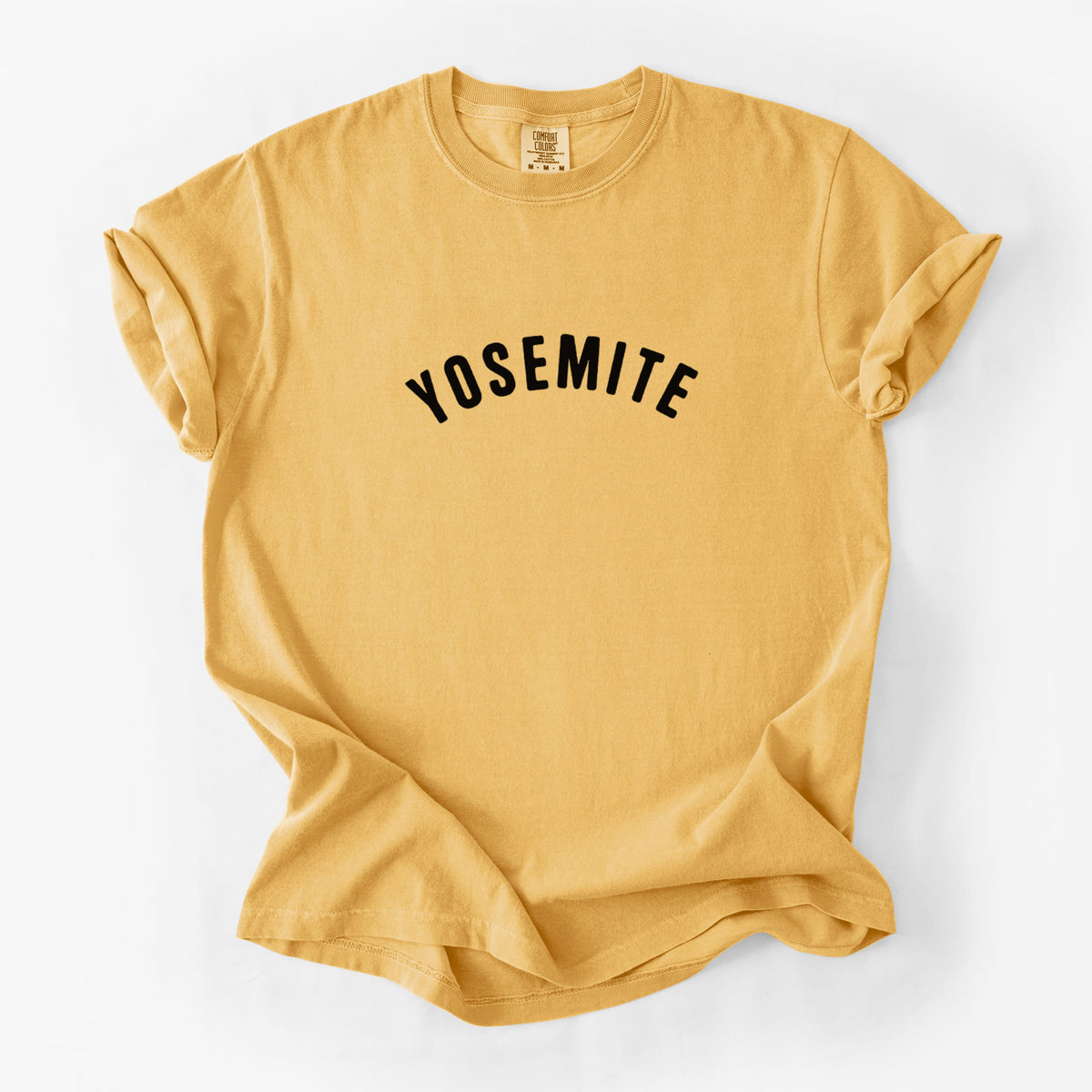Golden wheat yellow Comfort Colors t-shirt laid flat, printed with the word Yosemite in bold black letters arched across the chest.