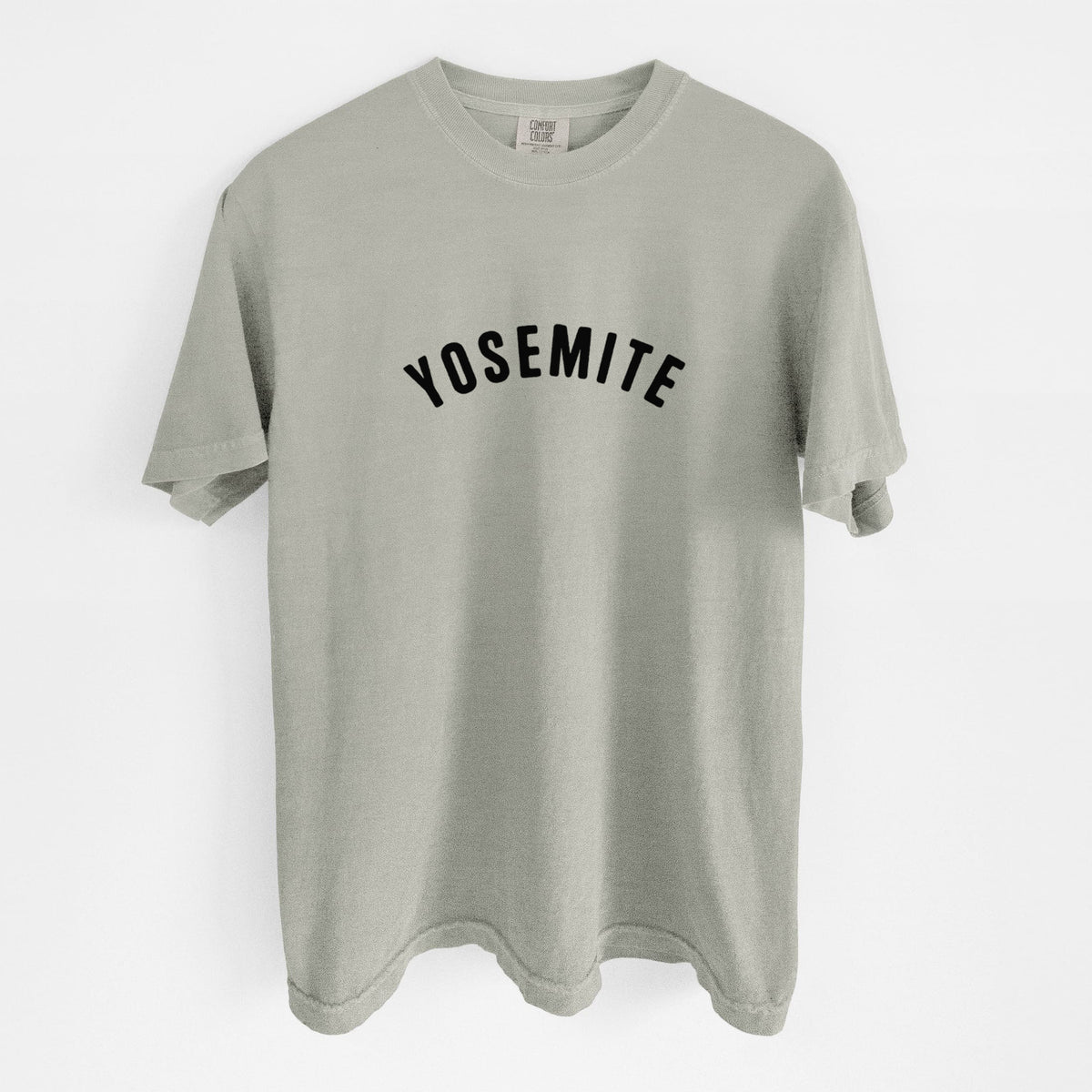 Sandstone beige Comfort Colors t-shirt laid flat, printed with the word Yosemite in bold black letters arched across the chest.