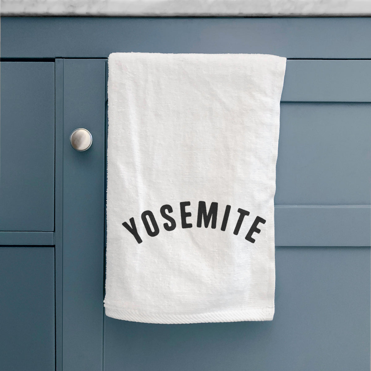 White hand towel printed with the word Yosemite in bold black letters arched across the chest, hanging on a cabinet door.
