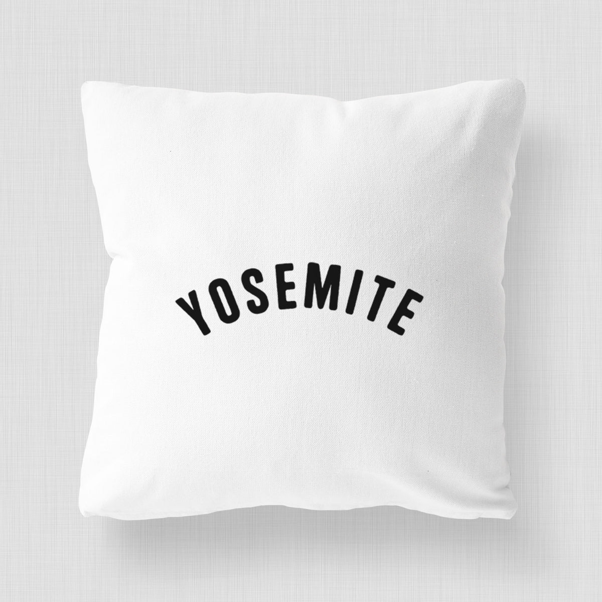 White pillow cover printed with the word Yosemite in bold black letters arched across the chest.