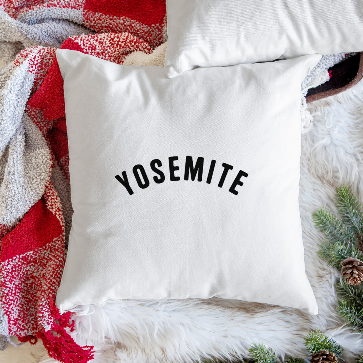 White pillow cover printed with the word Yosemite in bold black letters arched across the chest, on a woven chair.