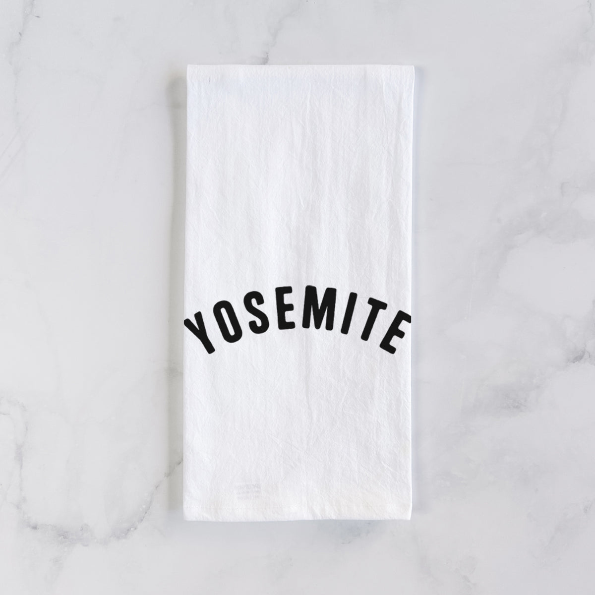 White cotton tea towel laid flat on marble, printed with the word Yosemite in bold black letters arched across the chest.