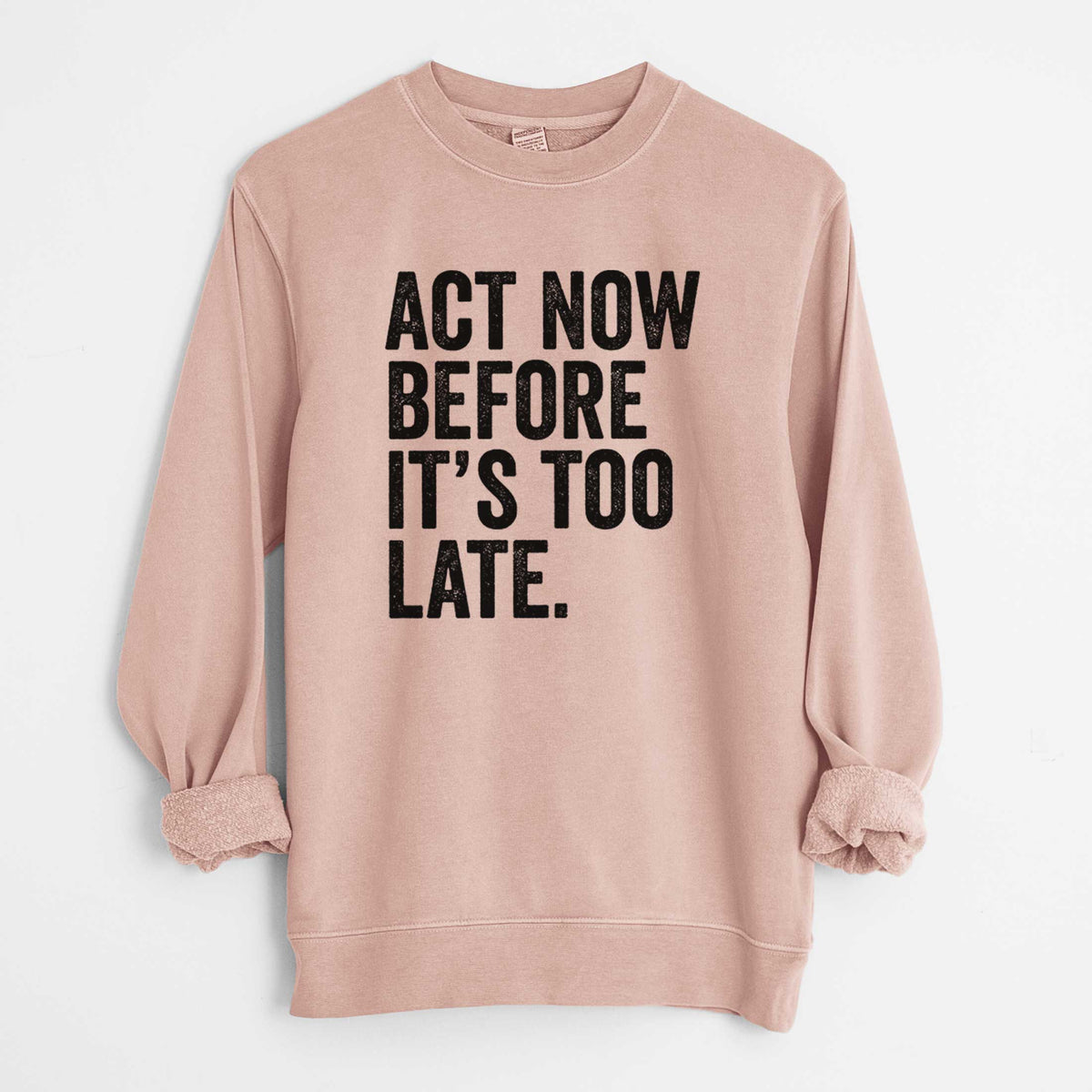 Dusty pink pigment dyed crewneck sweatshirt laid flat with the sleeves rolled, printed with bold black words reading Act Now Before It's Too Late.