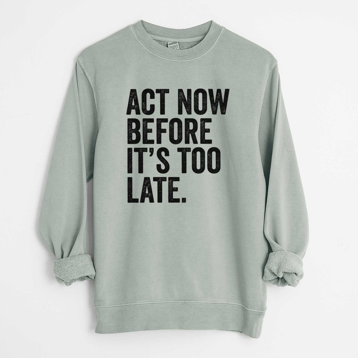Sage green pigment dyed crewneck sweatshirt laid flat with the sleeves rolled, printed with bold black words reading Act Now Before It's Too Late.