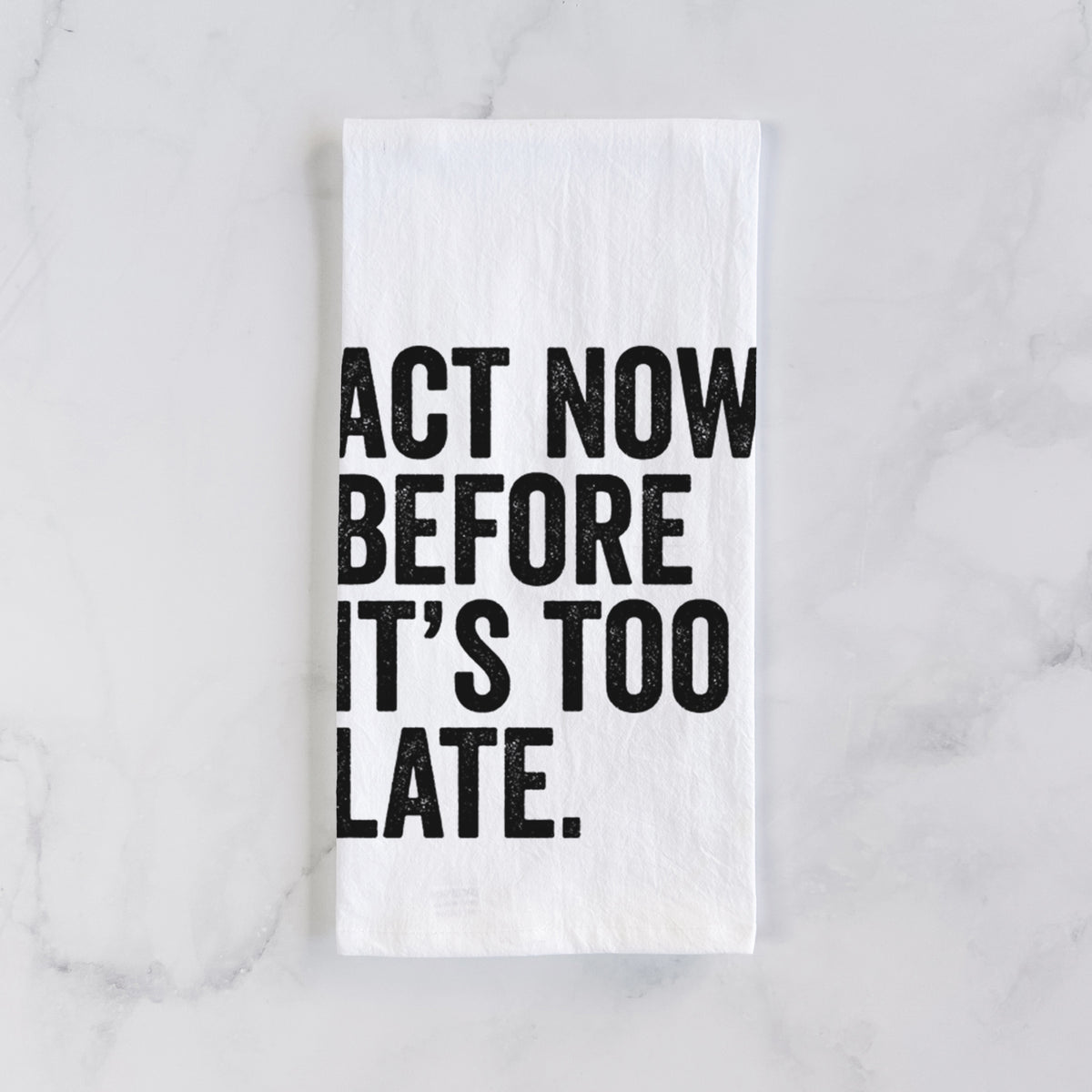 White cotton tea towel laid flat on marble, printed with bold black words reading Act Now Before It's Too Late.