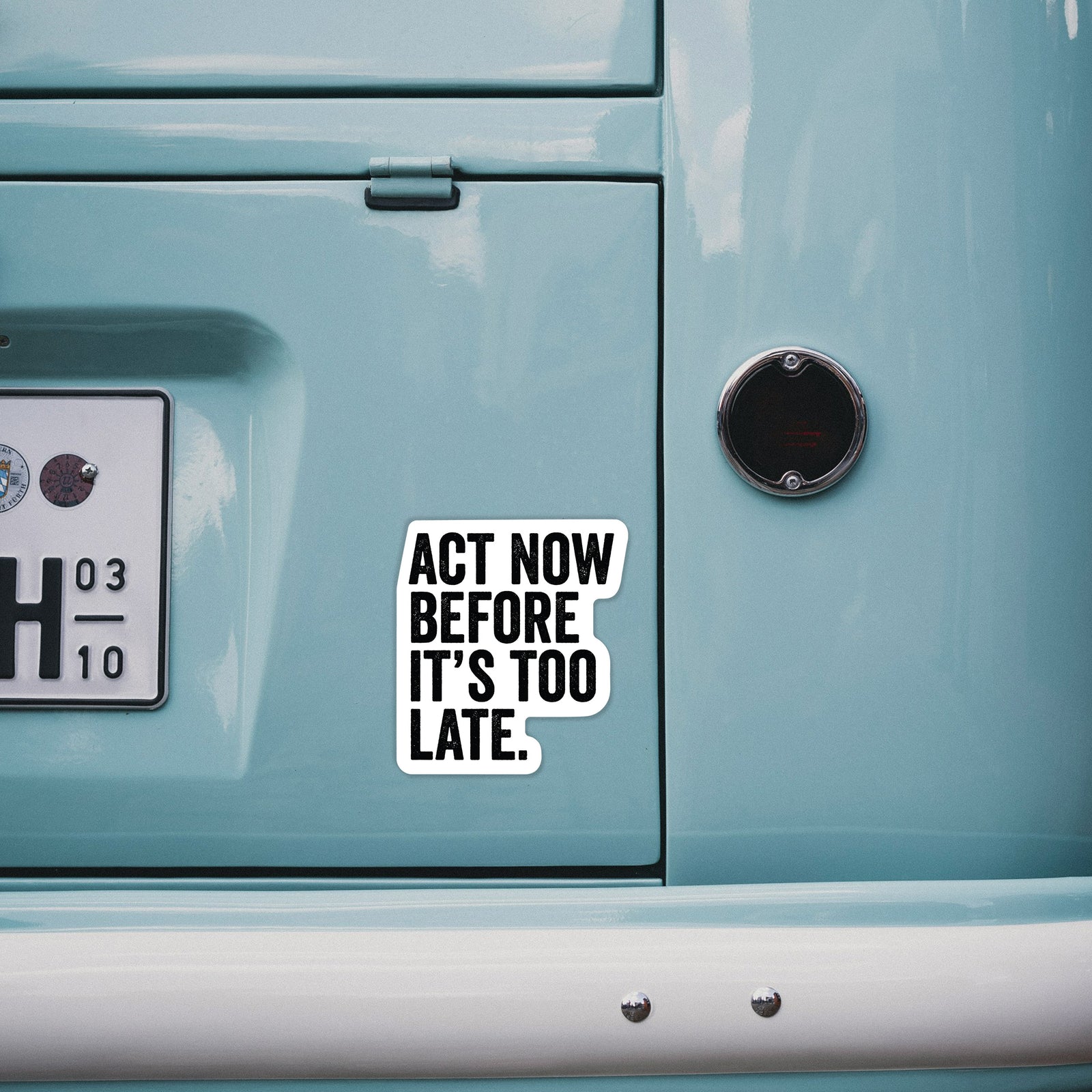 Hand holding a 4 inch vinyl decal of bold black words reading Act Now Before It's Too Late.