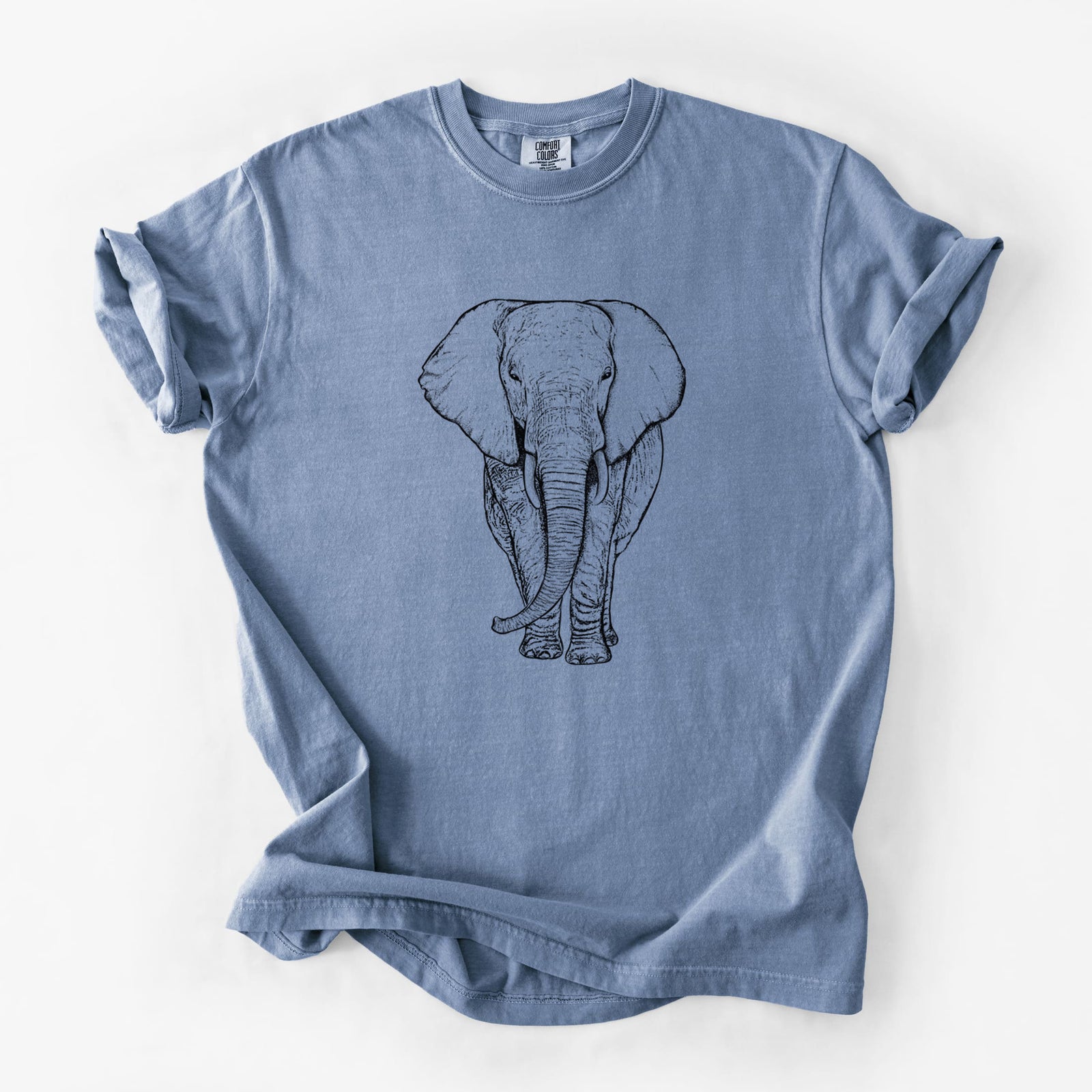 Blue jean Comfort Colors t-shirt laid flat, printed with a black ink line drawing of an African elephant facing forward with large ears and tusks.
