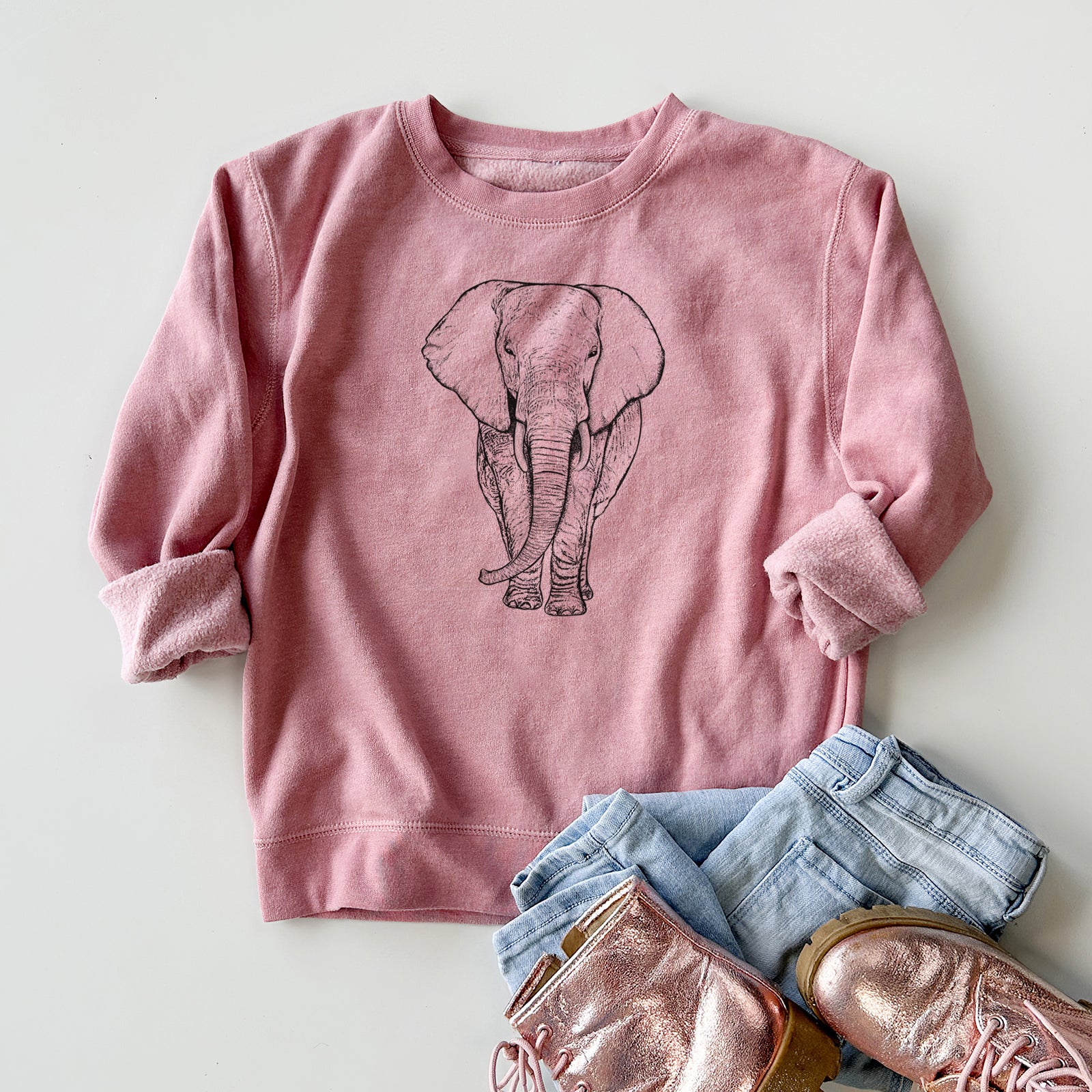 Boy wearing a youth crewneck sweatshirt printed with a black ink line drawing of an African elephant facing forward with large ears and tusks, outdoors.
