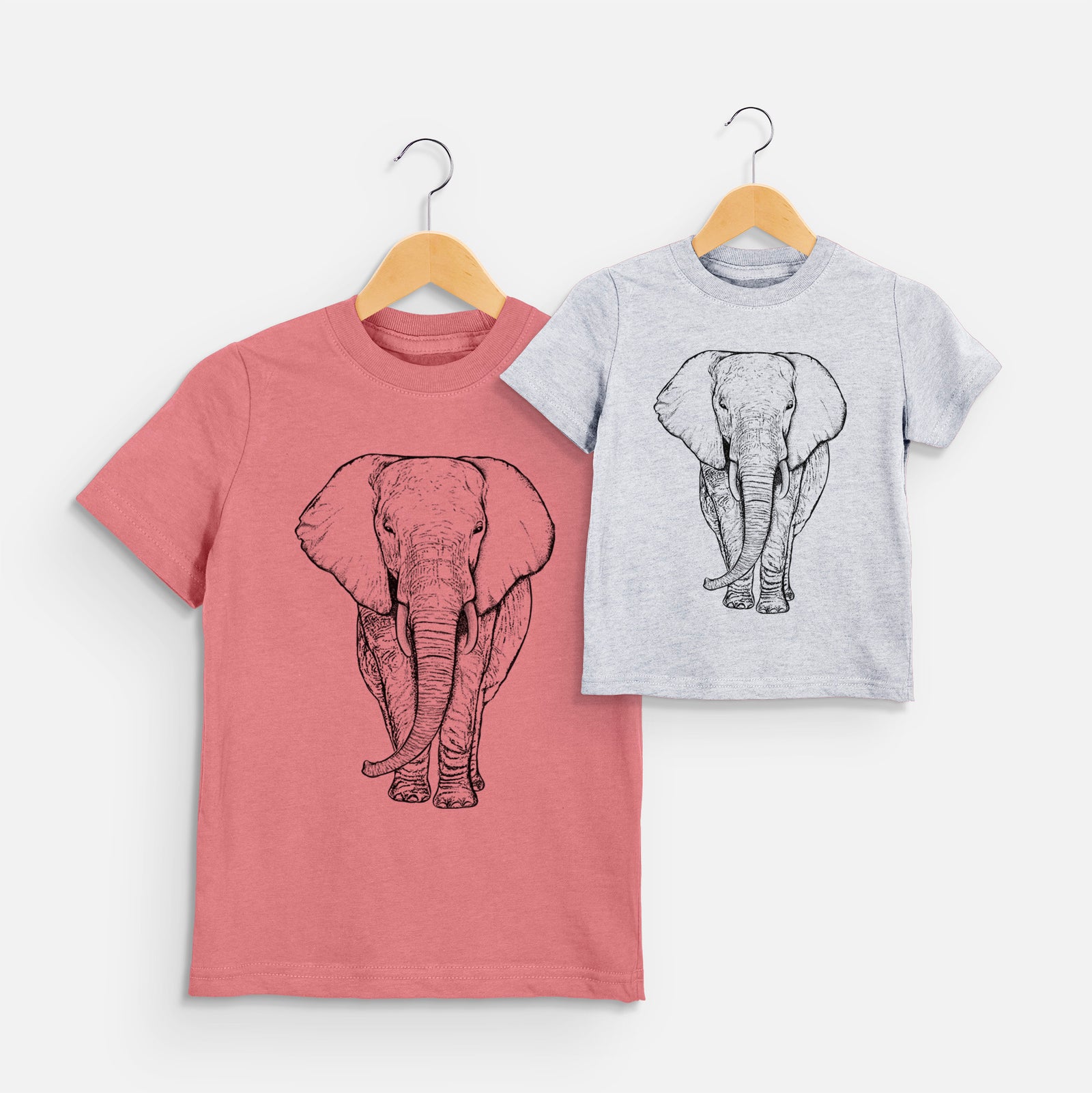 Two youth t-shirts in different colors on hangers, printed with a black ink line drawing of an African elephant facing forward with large ears and tusks.