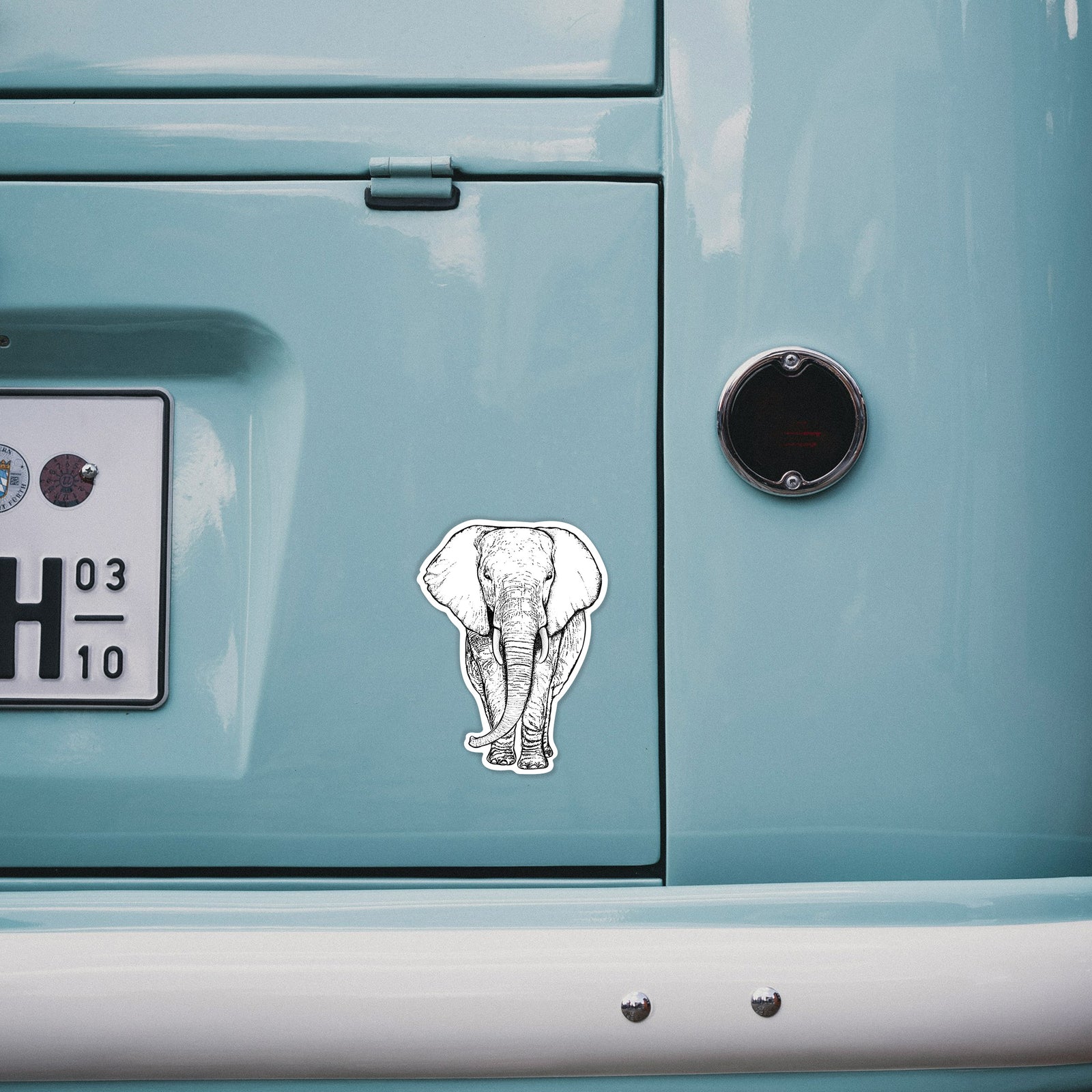 Hand holding a 4 inch vinyl decal of a black ink line drawing of an African elephant facing forward with large ears and tusks.