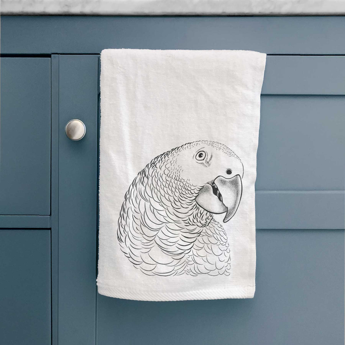 White hand towel printed with a detailed black ink portrait of an African grey parrot's head, hanging on a cabinet door.