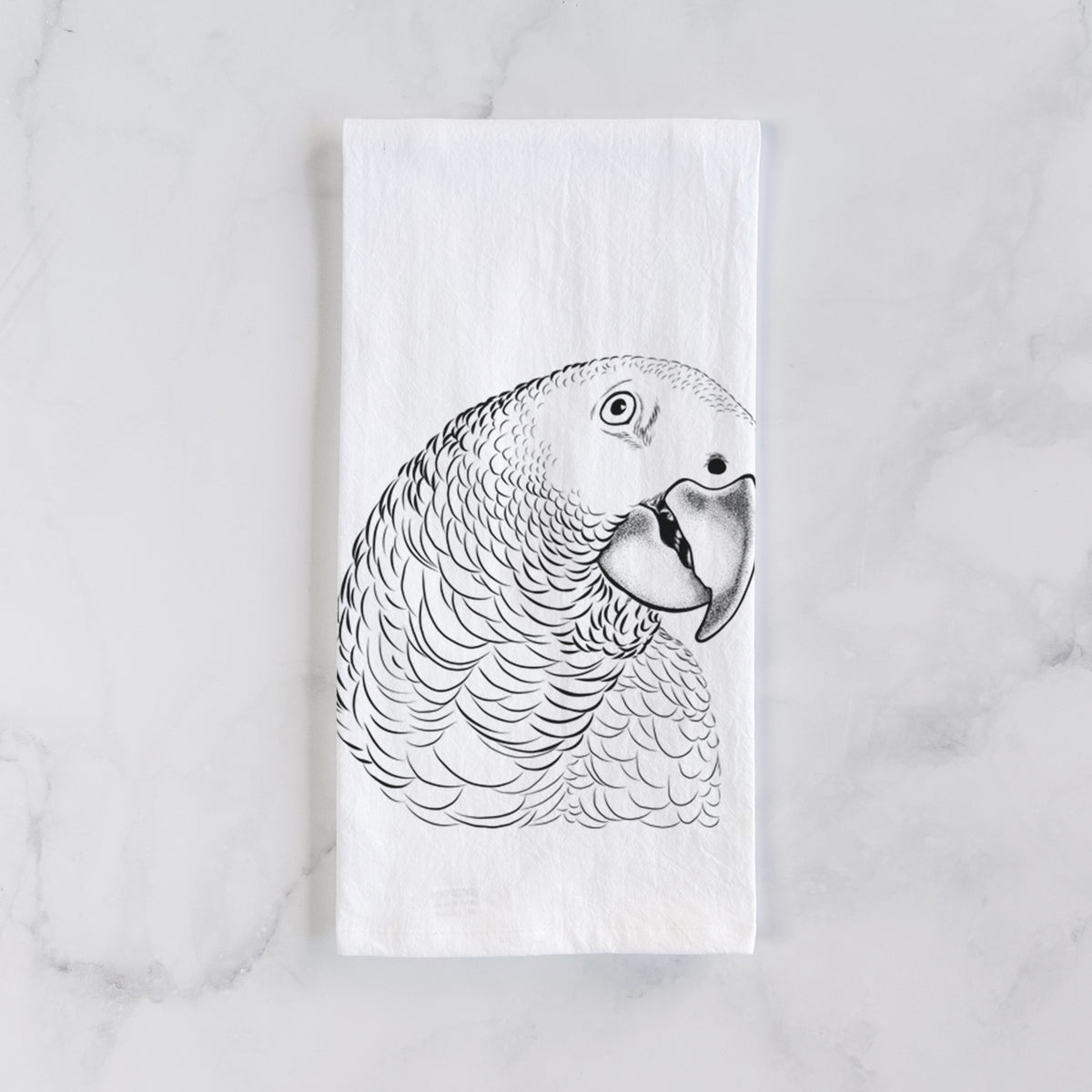 White cotton tea towel laid flat on marble, printed with a detailed black ink portrait of an African grey parrot's head.