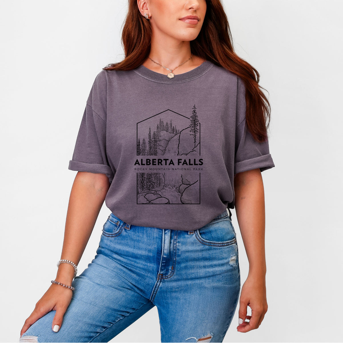 Woman wearing a Comfort Colors t-shirt printed with a black line art badge of Alberta Falls with pine trees, with the words Alberta Falls, Rocky Mountain National Park.