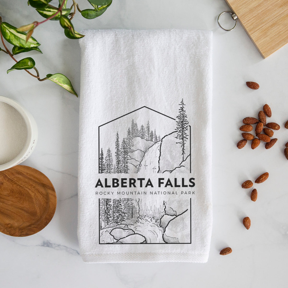 White hand towel printed with a black line art badge of Alberta Falls with pine trees, with the words Alberta Falls, Rocky Mountain National Park.