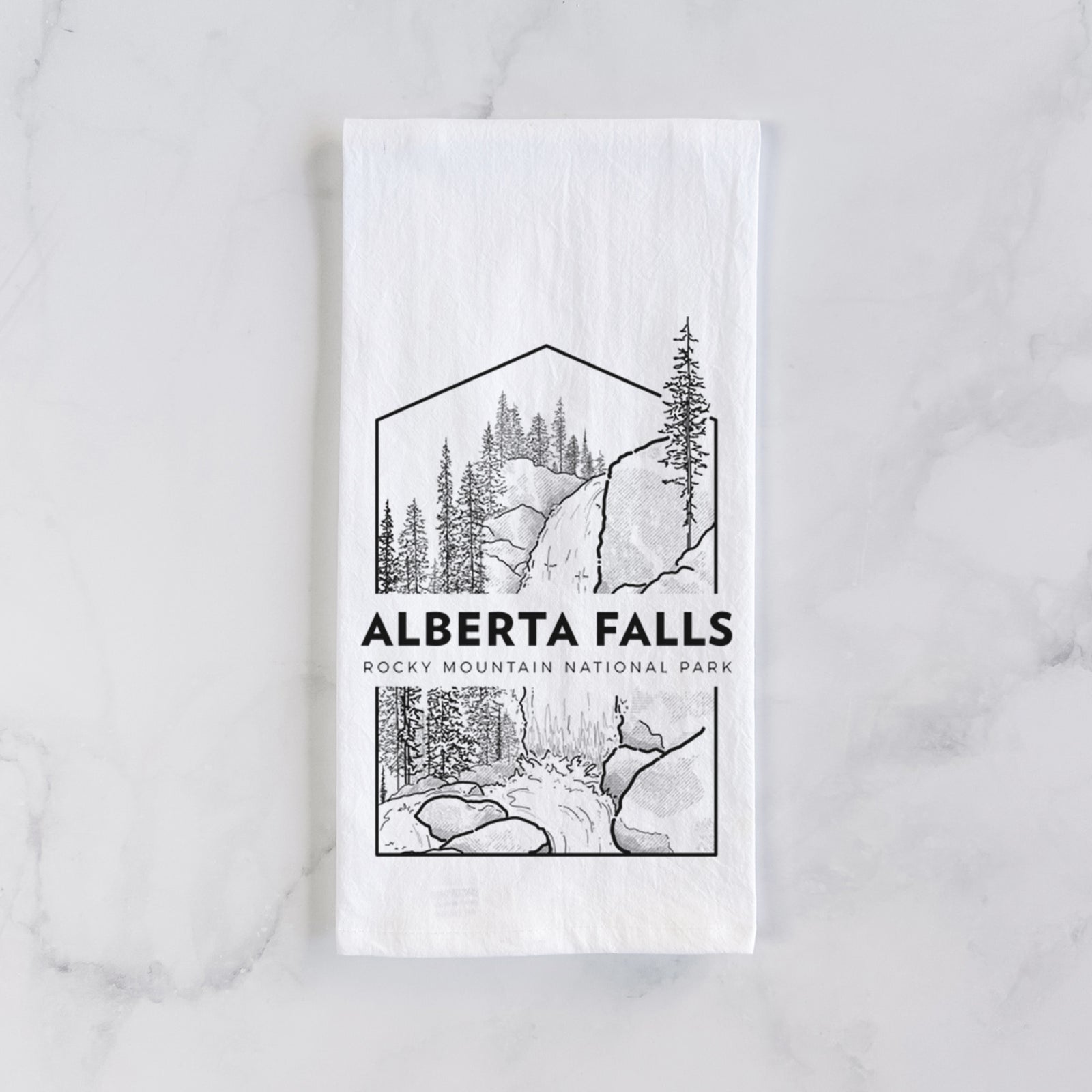 White cotton tea towel printed with a black line art badge of Alberta Falls with pine trees, with the words Alberta Falls, Rocky Mountain National Park, on a marble counter beside a round wooden cutting board and greenery.