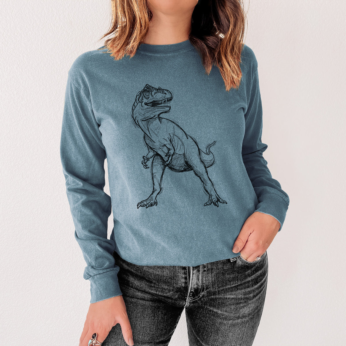 Steel blue Comfort Colors long sleeve shirt printed with a black ink illustration of an Allosaurus walking, shown in a lifestyle photo.