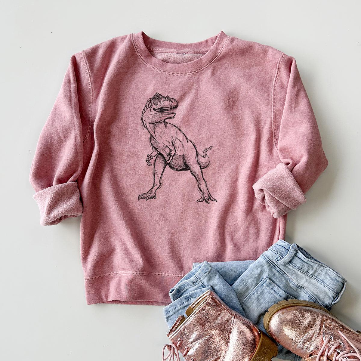 Youth crewneck sweatshirt printed with a black ink illustration of an Allosaurus walking, styled flat with jeans and boots.