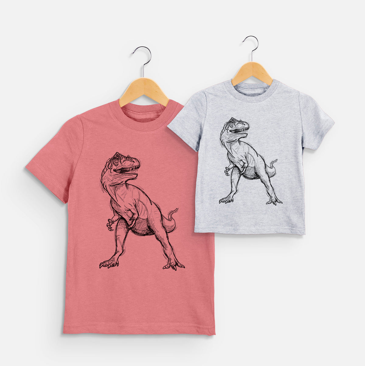 Two youth t-shirts in different colors on hangers, printed with a black ink illustration of an Allosaurus walking.