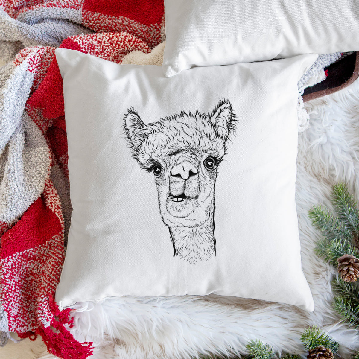 White pillow cover printed with a detailed black ink portrait of a fluffy alpaca's head and neck, on a woven chair.