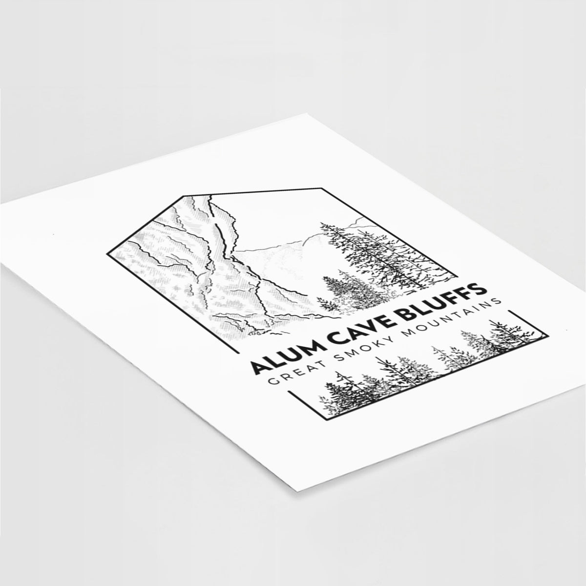 Art print of a black line art badge of Alum Cave Bluffs with pine trees, with the words Alum Cave Bluffs, Great Smoky Mountains, lying at an angle on a white surface.