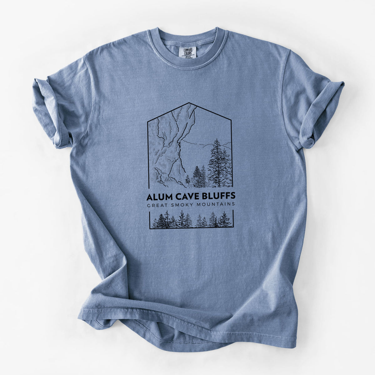 Blue jean Comfort Colors t-shirt laid flat, printed with a black line art badge of Alum Cave Bluffs with pine trees, with the words Alum Cave Bluffs, Great Smoky Mountains.