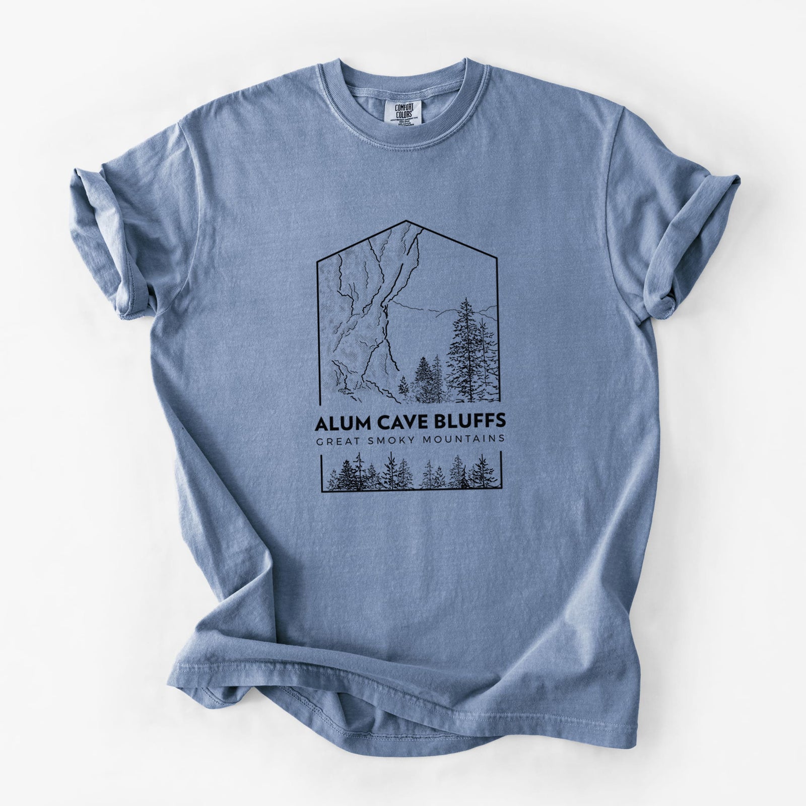 Blue jean Comfort Colors t-shirt laid flat, printed with a black line art badge of Alum Cave Bluffs with pine trees, with the words Alum Cave Bluffs, Great Smoky Mountains.