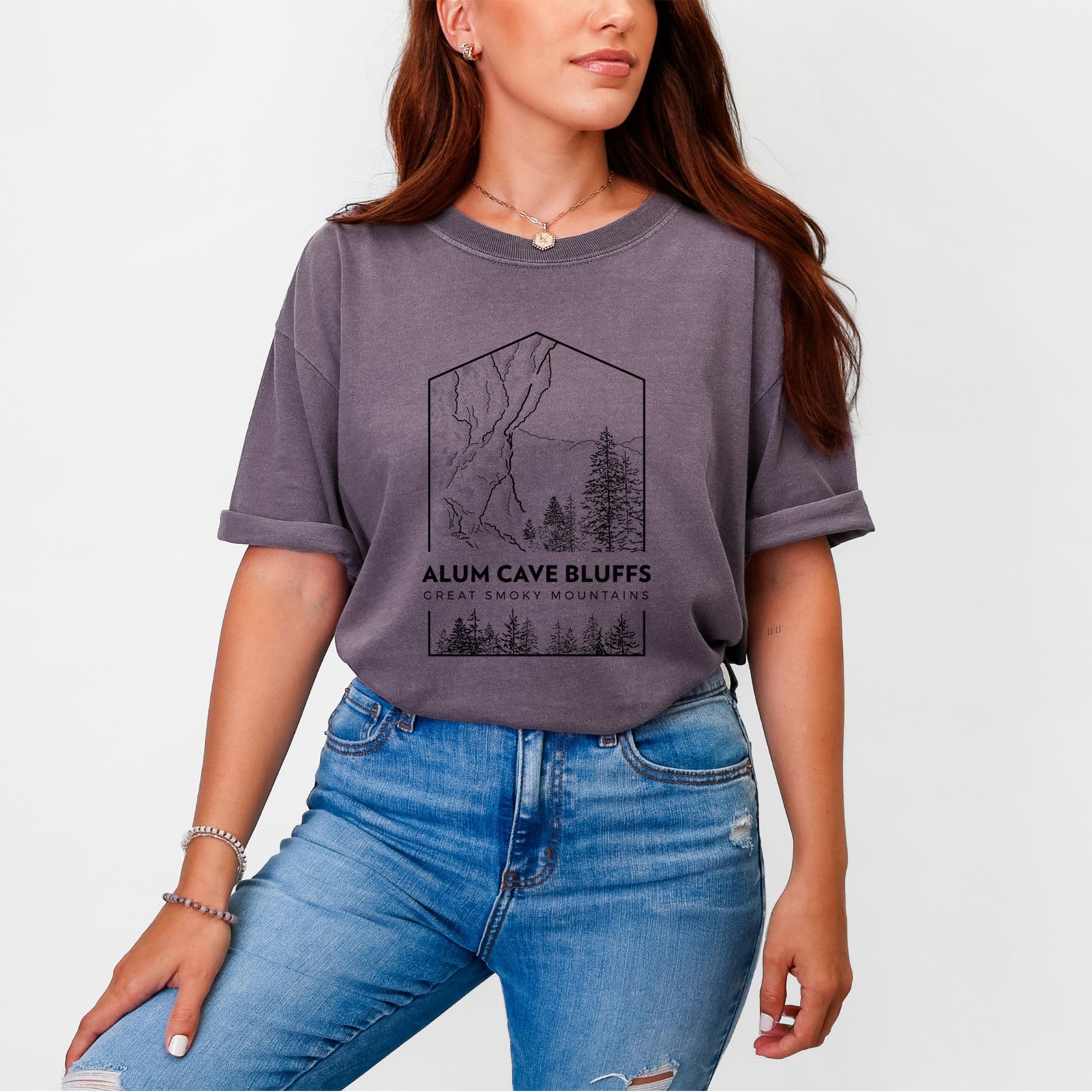 Blue jean Comfort Colors t-shirt laid flat, printed with a black line art badge of Alum Cave Bluffs with pine trees, with the words Alum Cave Bluffs, Great Smoky Mountains.