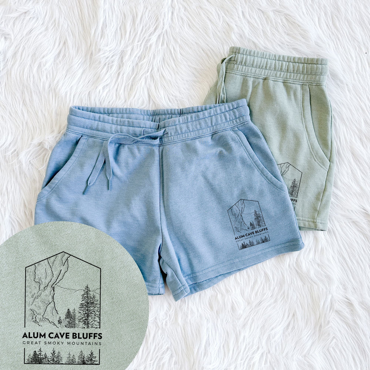 Two pairs of Cali Wave shorts in different colors printed with a black line art badge of Alum Cave Bluffs with pine trees, with the words Alum Cave Bluffs, Great Smoky Mountains, with a close-up of the print.