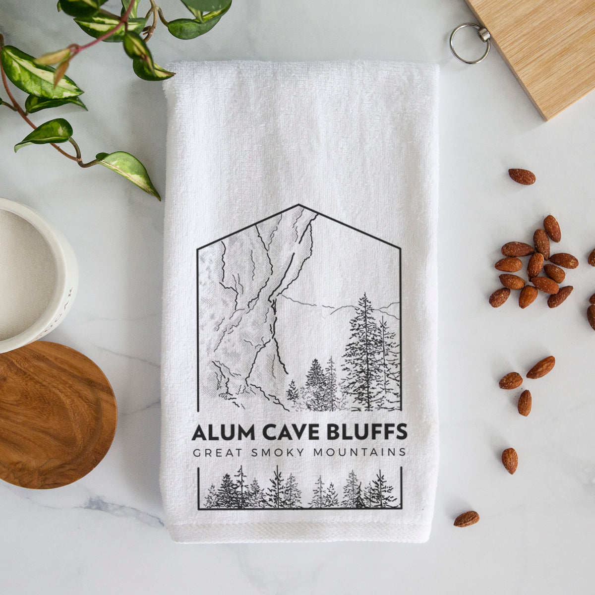White hand towel printed with a black line art badge of Alum Cave Bluffs with pine trees, with the words Alum Cave Bluffs, Great Smoky Mountains.
