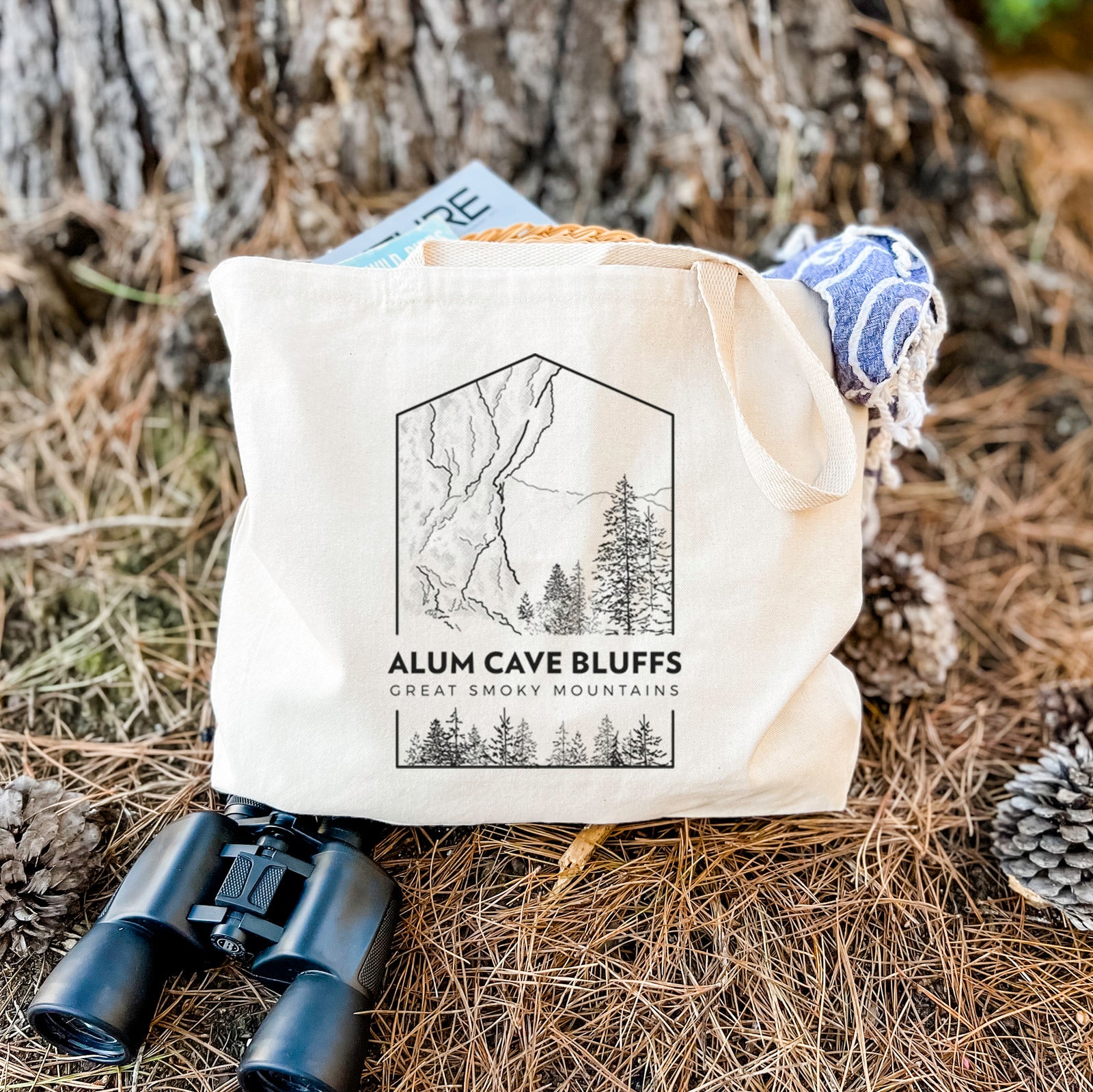 Natural canvas tote bag printed with a black line art badge of Alum Cave Bluffs with pine trees, with the words Alum Cave Bluffs, Great Smoky Mountains.