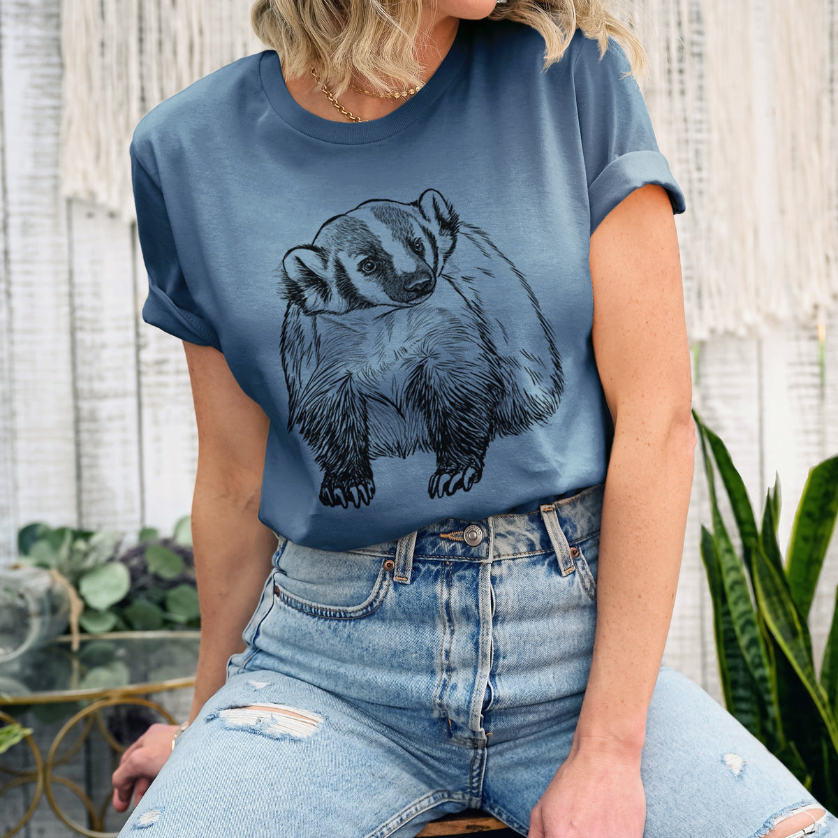 Woman wearing a steel blue lightweight cotton t-shirt printed with a detailed black ink illustration of an American badger facing forward.
