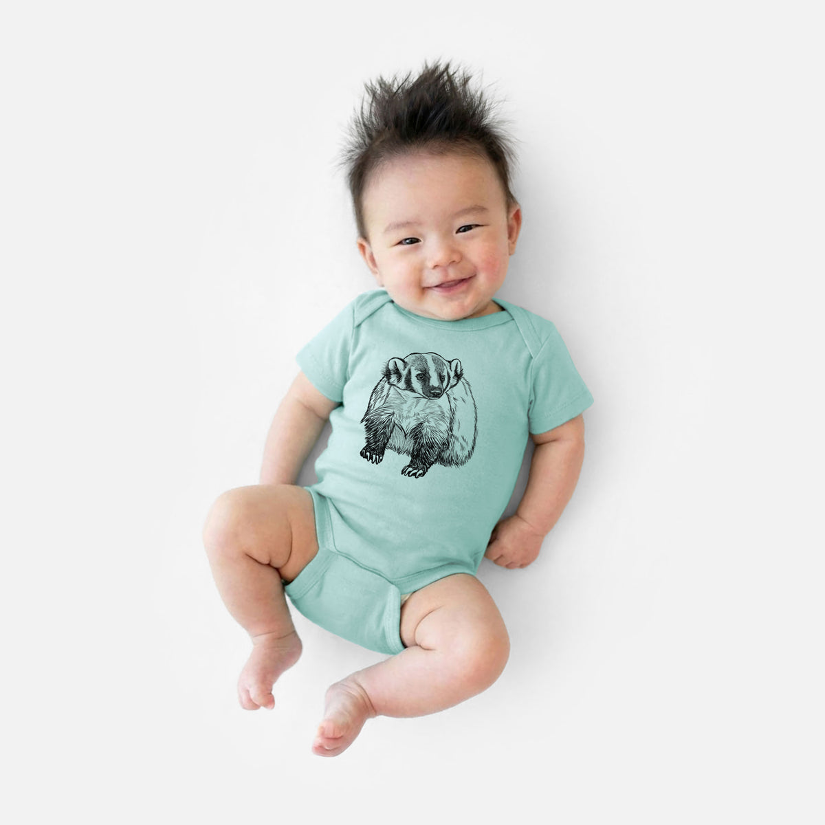 Smiling baby boy wearing a saltwater baby bodysuit printed with a detailed black ink illustration of an American badger facing forward.
