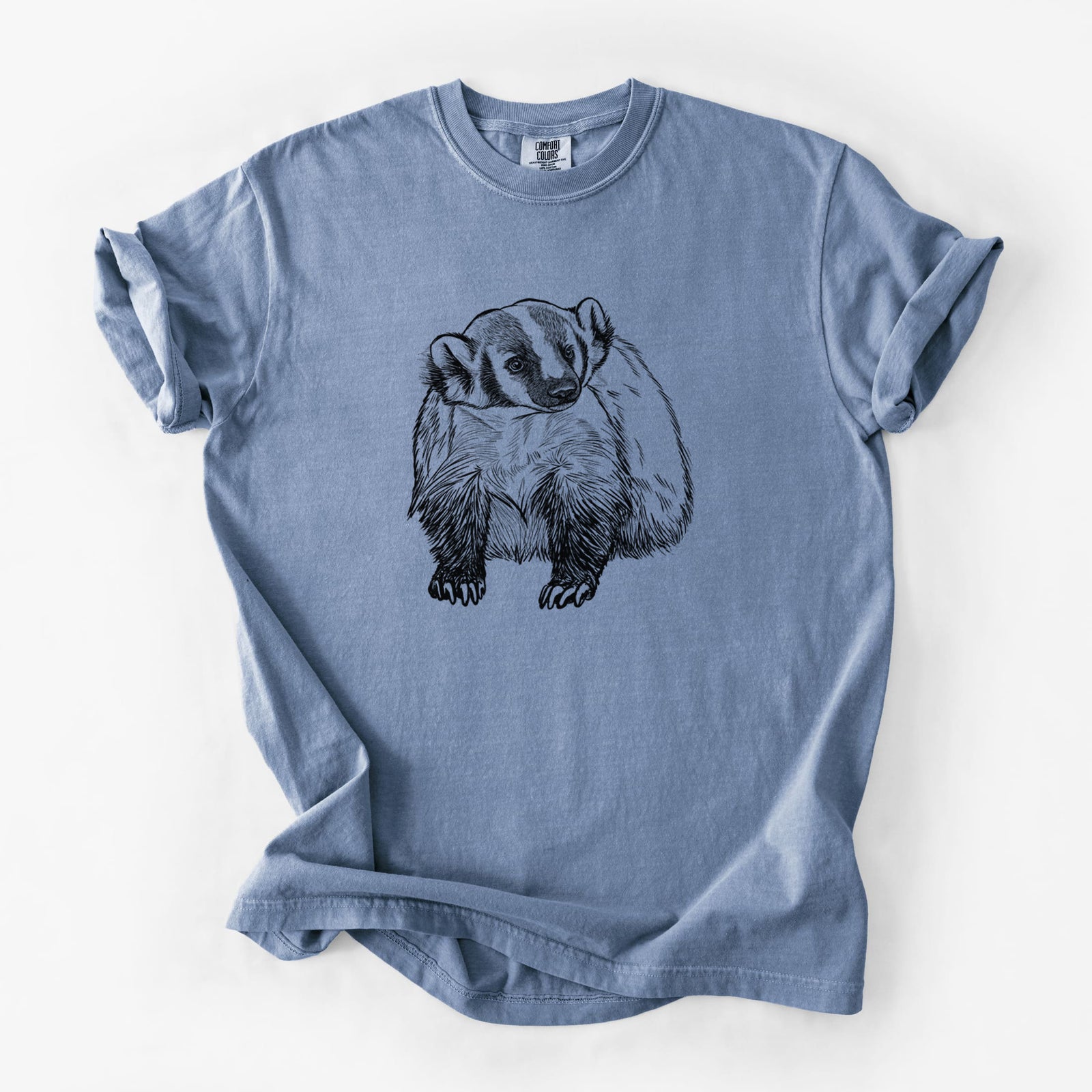 Blue jean Comfort Colors t-shirt laid flat, printed with a detailed black ink illustration of an American badger facing forward.