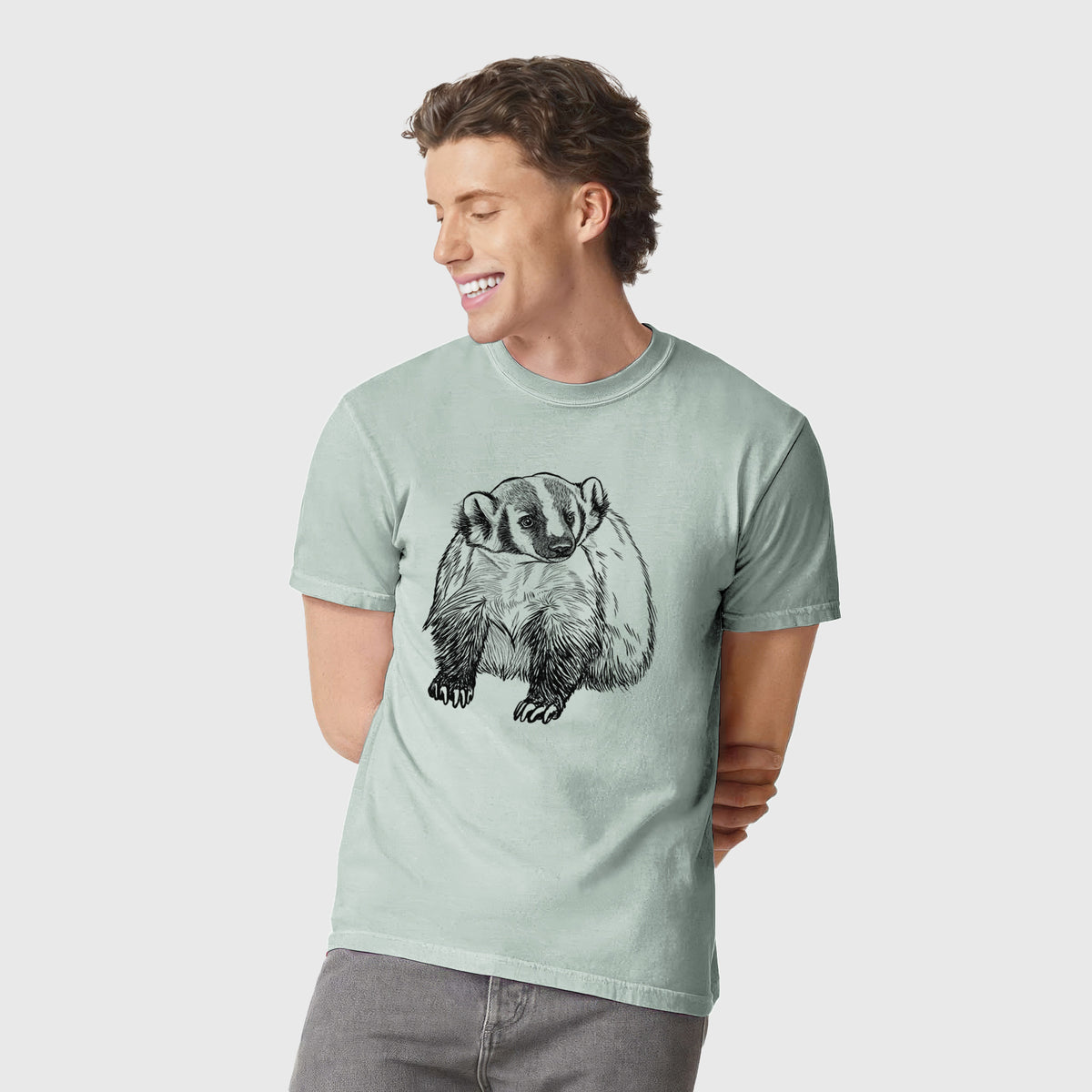 Man wearing a Comfort Colors t-shirt printed with a detailed black ink illustration of an American badger facing forward.