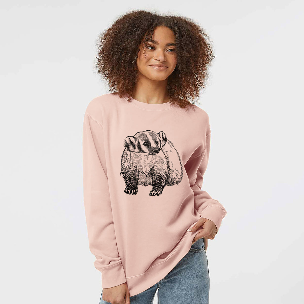 Model wearing a dusty pink pigment dyed crewneck sweatshirt printed with a detailed black ink illustration of an American badger facing forward.
