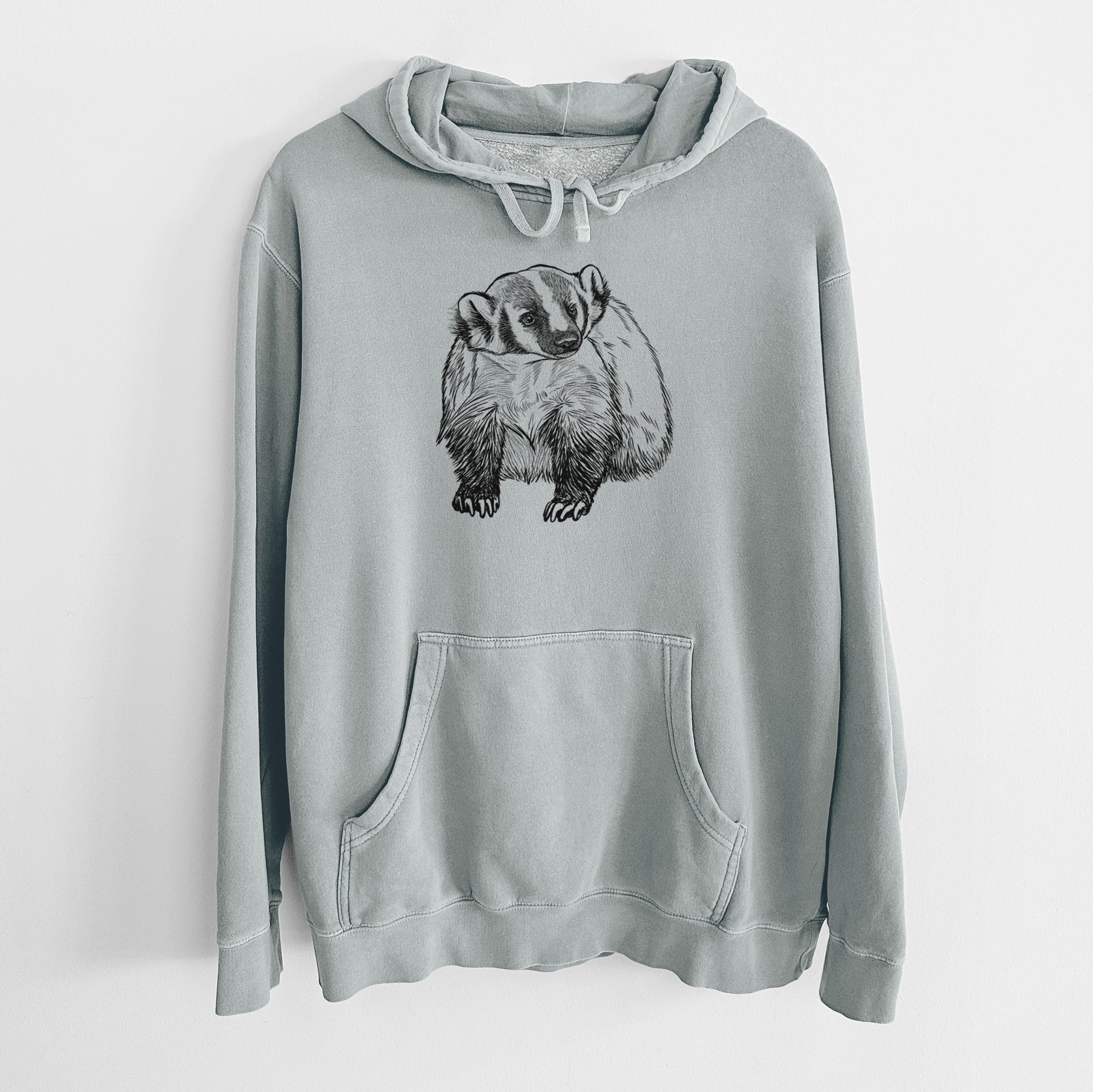Sage green pigment dyed hoodie laid flat, printed with a detailed black ink illustration of an American badger facing forward.