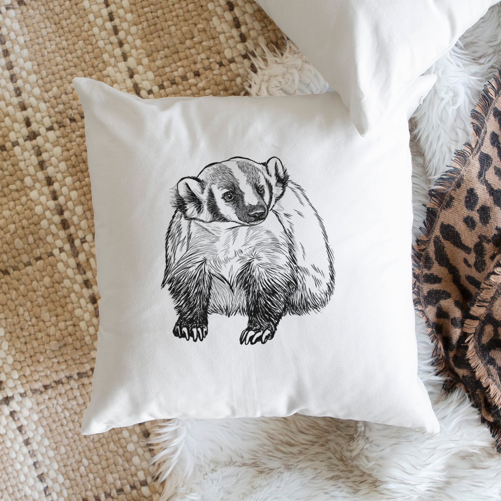 White pillow cover printed with a detailed black ink illustration of an American badger facing forward, on a bench beside plants.