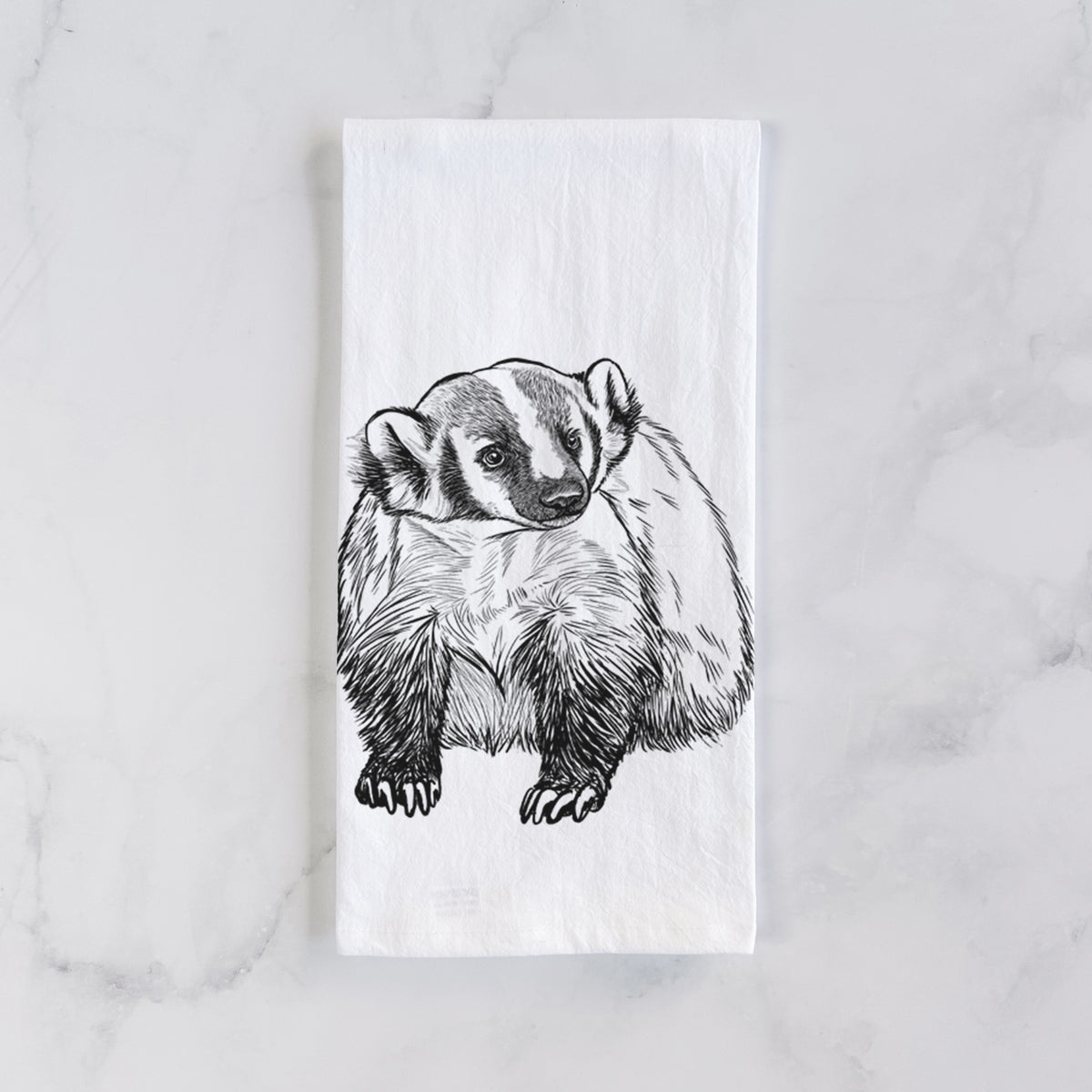 White cotton tea towel laid flat on marble, printed with a detailed black ink illustration of an American badger facing forward.