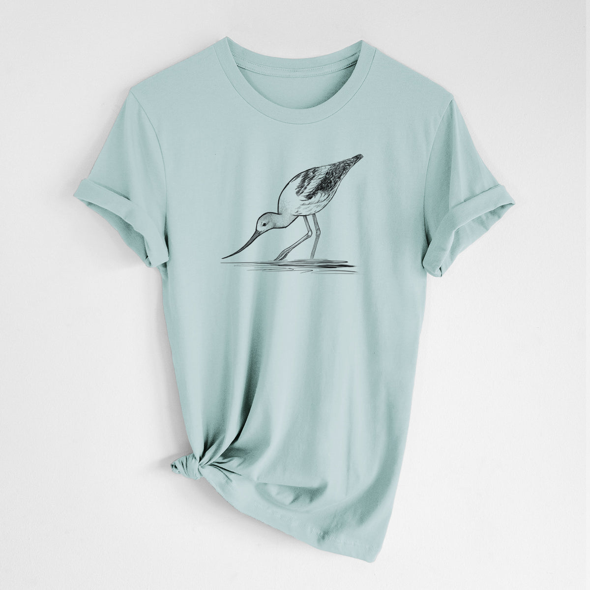 Dusty blue lightweight cotton t-shirt laid flat with the sleeves rolled, printed with a detailed black ink sketch of an American avocet wading in shallow water.