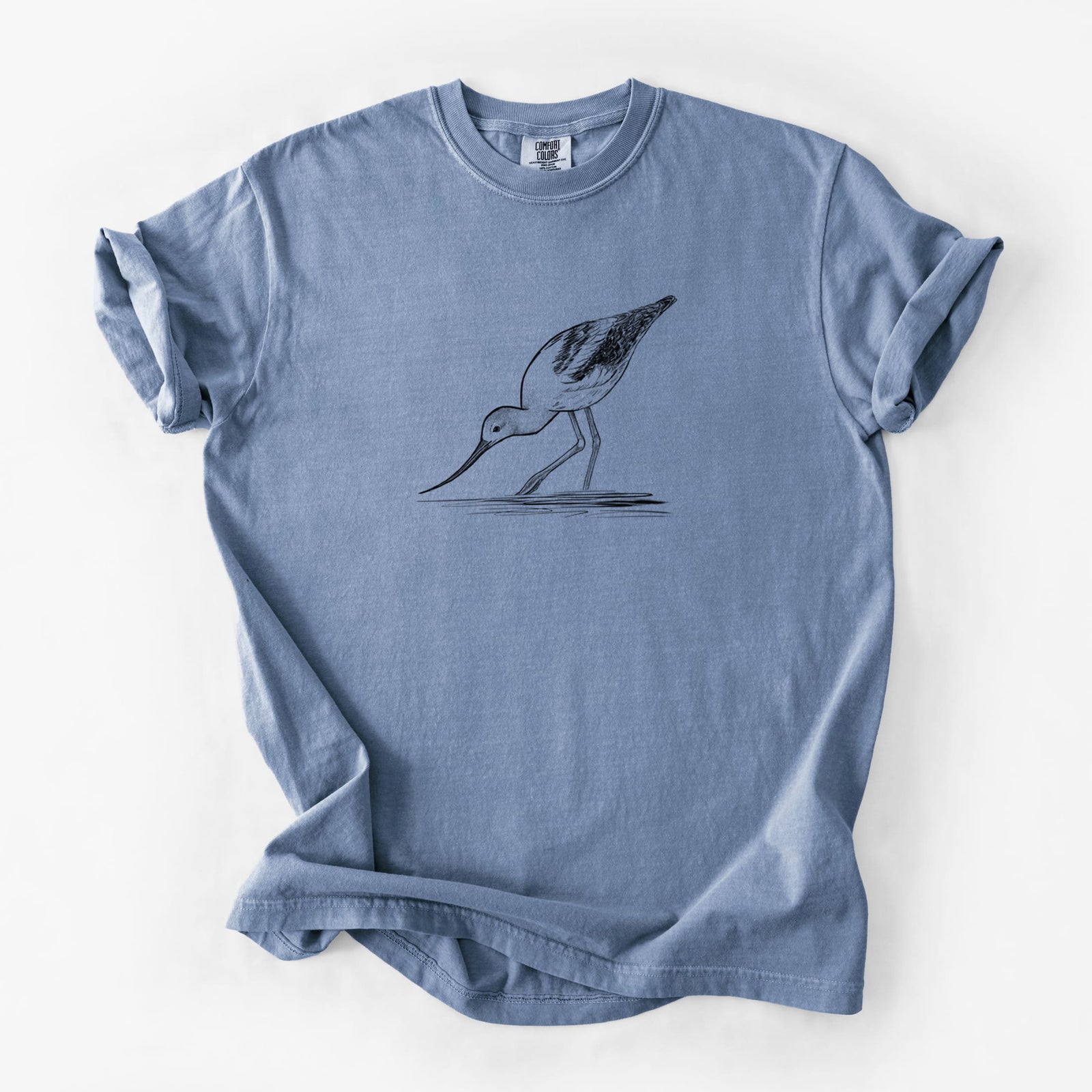Blue jean Comfort Colors t-shirt laid flat, printed with a detailed black ink sketch of an American avocet wading in shallow water.
