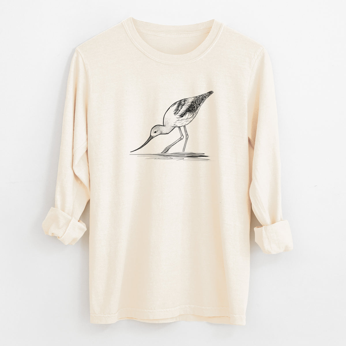 Ivory Comfort Colors long sleeve shirt laid flat with the cuffs rolled, printed with a detailed black ink sketch of an American avocet wading in shallow water.