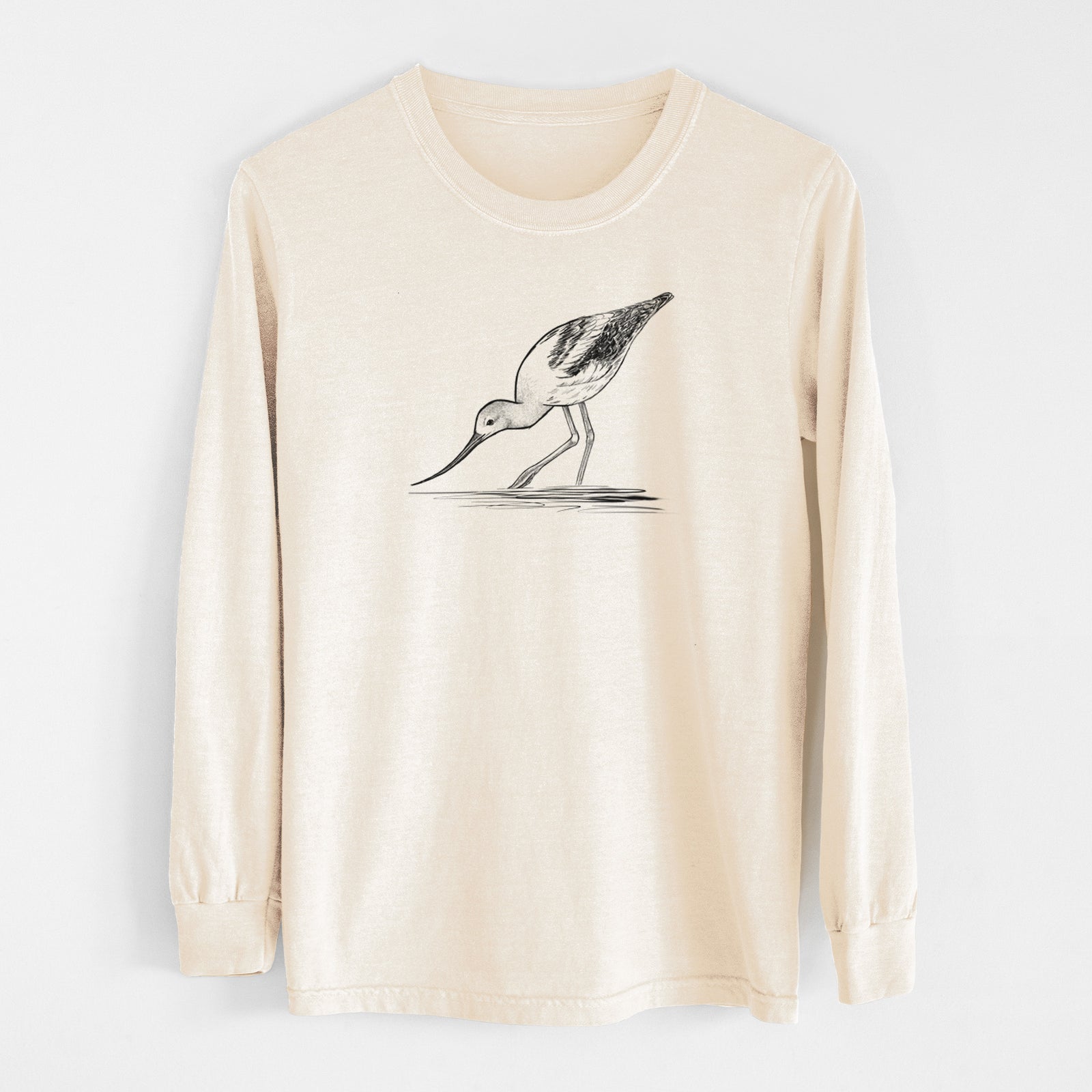 Ivory Comfort Colors long sleeve shirt laid flat, printed with a detailed black ink sketch of an American avocet wading in shallow water.