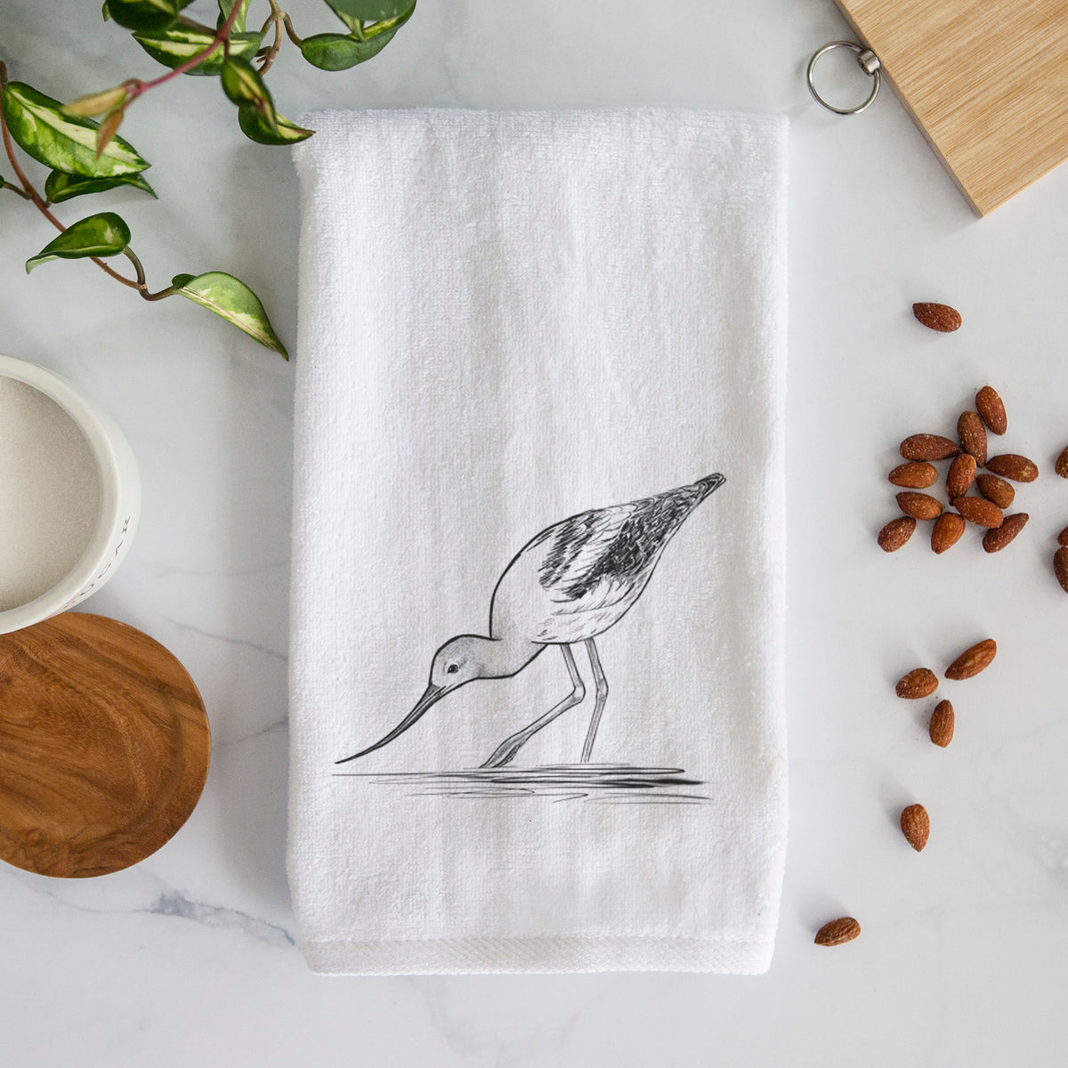 White hand towel printed with a detailed black ink sketch of an American avocet wading in shallow water.