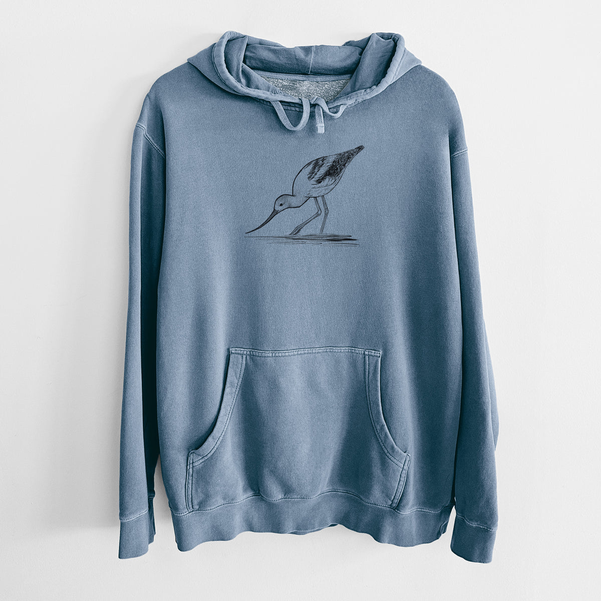 Slate blue pigment dyed hoodie laid flat, printed with a detailed black ink sketch of an American avocet wading in shallow water.