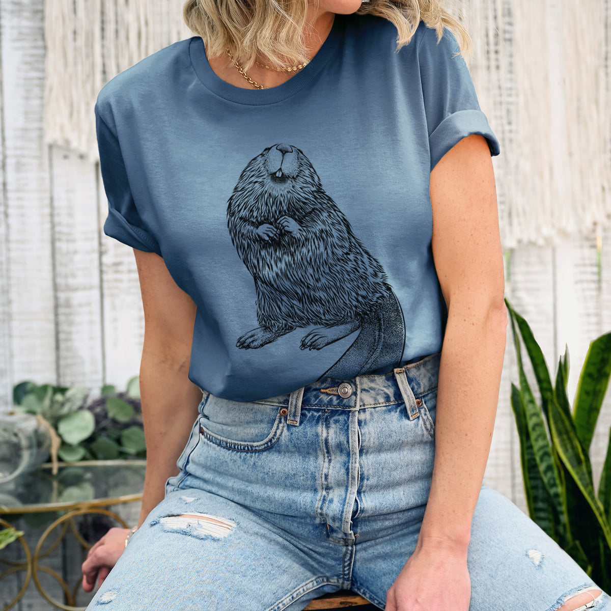 Woman wearing a steel blue lightweight cotton t-shirt printed with a detailed black ink illustration of an American beaver sitting upright with its flat tail.