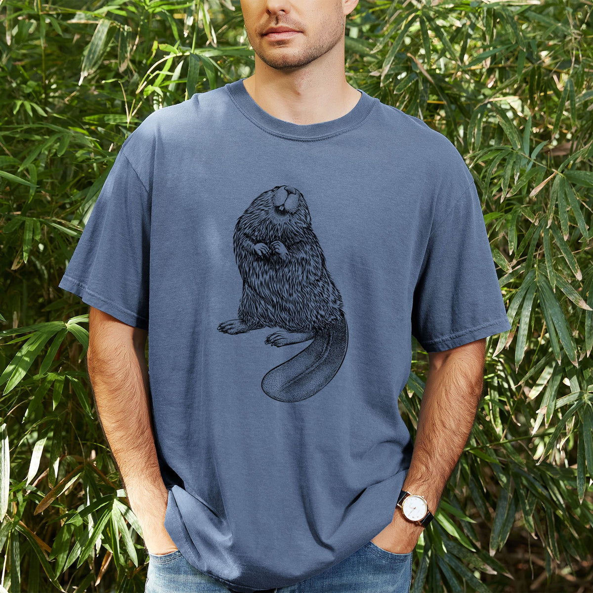 Man wearing a Comfort Colors t-shirt printed with a detailed black ink illustration of an American beaver sitting upright with its flat tail, outdoors.